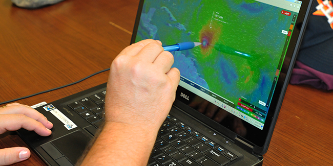 Majumdar-DynamicGraphics Pointing at a laptop screen with image of a storm.