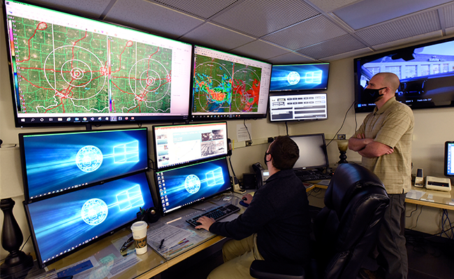 Forecaster sits in office with multiple screens showing various forecasts